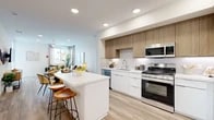 Located at 1604 W Lincoln Ave in Anaheim, CA, this well-appointed 2-bedroom, 2-bathroom residence offers a thoughtfully designed single-level floor plan with a bright, contemporary aesthetic throughout. Light wood-tone flooring flows seamlessly across the entire space, lending warmth and visual continuity.

The open-concept kitchen is a standout feature, showcasing a two-tone cabinetry design with white lower cabinets and natural wood upper cabinets, complemented by a white quartz countertop island with bar seating. Stainless steel appliances—including a gas range, built-in microwave, dishwasher, and French door refrigerator—complete the modern kitchen suite. Recessed lighting illuminates the space efficiently.

The kitchen opens directly into the living area, which benefits from large windows that invite abundant natural light. A private balcony extends the living space outdoors, offering pleasant views of the surrounding neighborhood.

The primary bedroom is a comfortable retreat with a well-sized walk-in closet featuring built-in shelving and hanging rods. A second bedroom offers similar finishes and generous closet access. Both bathrooms are clean and modern, with white cabinetry and wood-look flooring. Two dedicated closets provide ample storage throughout the residence.