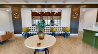 Located on Wildwood Cir in Homewood, Alabama, this single-story community clubhouse blends modern farmhouse aesthetics with functional, multi-use spaces designed for gathering and connection. The interior is unified by warm wood-plank flooring laid in a herringbone pattern, soaring vaulted ceilings clad in rich tongue-and-groove wood planking, and exposed beams that lend an open, airy character throughout.

The main lounge area features a built-in banquette upholstered in classic buffalo check, accented by bold yellow and green throw pillows, surrounding a round wood-top table — all set against dark shiplap walls and a large mirrored partition. An adjacent seating lounge offers a circle of plush armchairs centered around a low coffee table beneath a statement pendant light, with large windows and glass doors inviting abundant natural light and outdoor views.

A dedicated dining and work area provides a long communal table with industrial-style seating beneath Edison bulb pendants, complemented by teal cabinetry and a glass partition wall. A striking conference room showcases a dramatic floor-to-ceiling Birmingham area map mural, flanked by vaulted ceilings and fitted with a long table and navy upholstered chairs. A well-appointed mail room with a central island workstation and built-in mailboxes rounds out the amenities of this thoughtfully designed community space.