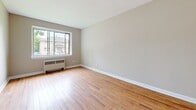 Located on Hollington Street in Ottawa, this single-floor 2-bedroom, 1-bathroom unit offers a functional and efficiently designed living space. Warm hardwood flooring flows throughout the main living areas and both bedrooms, creating a cohesive and inviting atmosphere.

The primary bedroom is a comfortable size, featuring a built-in closet with upper storage, neutral warm-grey walls, and a window that allows natural light to fill the room. The second bedroom also features hardwood floors and a built-in wardrobe, providing practical storage.

The kitchen is well-appointed with a two-tone design, combining dark wood lower cabinets and crisp white upper cabinetry. Light stone-effect countertops, a stainless steel sink, a stainless steel electric range, and an overhead exhaust fan complete this functional cooking space. The floor transitions to tile in the kitchen area.

The bathroom is clean and simply designed, with white wall tiles accented by black square details, a vanity with under-sink storage, a full bathtub, and warm beige floor tiles.

The main living area benefits from a large window overlooking the surrounding neighbourhood, with a radiator heating unit positioned beneath it. The overall space maintains a bright, neutral palette throughout, making it a practical and comfortable residence.
