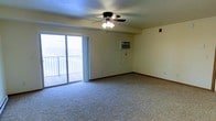 This single-floor space offers a clean, functional layout designed for comfortable everyday living. The main living area is generously sized, featuring wall-to-wall carpeting that adds warmth and softness underfoot. A ceiling fan with an integrated light fixture is centrally mounted, providing both air circulation and ambient lighting throughout the room. A wall-mounted air conditioning unit ensures climate control year-round. One of the standout features of the living area is the large sliding glass door, which floods the space with natural light and provides direct access to a private balcony. The balcony overlooks an expansive open view, offering a bright and airy atmosphere that extends the feel of the interior outward. The neutral, light-toned walls throughout the space create a versatile backdrop, making it easy to personalize with furnishings and décor. Baseboards and standard ceiling height give the space a straightforward, practical character. Overall, the layout is open and unobstructed, allowing for flexible furniture arrangements and a comfortable sense of space throughout.