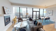 This elegantly appointed high-rise residence offers a seamless blend of contemporary design and elevated urban living. The open-plan living and dining area serves as the heart of the home, anchored by a sleek wall-mounted fireplace and floor-to-ceiling windows that frame sweeping city skyline views. Light hardwood flooring flows throughout the main living spaces, complemented by refined furnishings in neutral tones with rich teal and navy accents.

The gourmet kitchen is outfitted with premium stainless steel appliances, including a professional-grade range and a large French door refrigerator. Crisp white cabinetry extends to the ceiling, providing generous storage, while a window above the counter brings in natural light and additional skyline views.

The primary bedroom is a serene retreat, featuring expansive floor-to-ceiling glass doors opening to a private balcony with commanding city views and plush carpeting underfoot. A generously sized walk-in closet with custom built-in shelving and drawers offers exceptional organization. The bathrooms are finished in clean white subway tile, with one featuring a soaking tub and glass-enclosed shower.

A dedicated laundry room houses a full-sized washer and dryer. A well-appointed powder room and an additional bedroom round out this thoughtfully designed residence.
