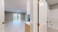 This efficiently designed single-floor unit offers a thoughtful open-concept layout that combines the kitchen and living area into one cohesive space. The kitchen is well-appointed with stainless steel appliances, including a full-size refrigerator, electric range with overhead ventilation, and a dishwasher. Cabinetry features a two-tone design pairing crisp white upper cabinets with warm natural wood lower cabinets, complemented by light quartz countertops and black hardware accents. Recessed lighting illuminates the kitchen workspace effectively.

The living area is bright and airy, finished with light hardwood-style flooring that flows throughout the unit, soft gray walls, and clean white baseboards. A wall-mounted split-system air conditioning unit provides climate control, and recessed ceiling lights add to the modern aesthetic. A sliding glass door opens to a private balcony, allowing natural light to fill the room and offering views of the surrounding building exterior.

In-unit stacked laundry and utility panels are neatly tucked away in a dedicated closet space within the living area. The full bathroom features a soaking tub with shower, a wood-toned vanity with white countertop and black hardware, a toilet, and neutral tile flooring, maintaining the unit's consistent modern design language.