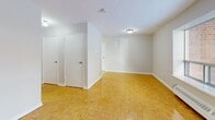 Located at 12 Park St E in Mississauga, Ontario, this efficiently designed unit offers a practical and well-organized layout across a single floor. The combined living and dining area serves as the heart of the space, featuring warm, polished parquet flooring in a classic basket-weave pattern that extends throughout the unit. A large picture window allows natural light to fill the room while offering views of the surrounding neighbourhood, complemented by a baseboard heating unit beneath the sill. The neutral grey walls and white trim provide a clean, bright backdrop throughout.

The kitchen is outfitted with white cabinetry, ample counter space, and essential appliances, including a stove and sink, making it a functional workspace despite its compact footprint. The bathroom is finished in a crisp, all-white palette, featuring a full-sized soaking tub with an overhead shower, a pedestal-style vanity with cabinet storage, a medicine cabinet mirror, and light tile flooring.

The entrance provides a welcoming transition into the unit, and three closets offer generous storage options — a practical feature in a space of this scale. The overall ambiance is clean, neutral, and move-in ready, making it a straightforward and functional urban residence in the heart of Mississauga.