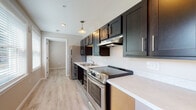 Located at 31 Village Ln in Groton, Connecticut, this single-floor unit offers a clean, contemporary design with thoughtful finishes throughout. The kitchen is a standout feature, outfitted with dark espresso shaker-style cabinetry, light quartz countertops, stainless steel appliances including a range and refrigerator, an undermount sink, and pendant lighting that adds a warm, stylish touch. Light-toned hardwood-style flooring runs consistently throughout the unit, creating a cohesive and open feel.

The living and bedroom areas are bright and open, with neutral warm-toned walls, recessed lighting, and large windows in the main living space that invite natural light and views of the surrounding neighborhood. A wall-mounted mini-split unit provides efficient climate control. The spacious, minimalist layout allows for flexible furniture arrangements.

The bathroom is designed with accessibility in mind, featuring grab bars near the shower and toilet, a roll-under vanity with a wide sink, a walk-in shower with a curtain rod, and a framed medicine cabinet. The light flooring and neutral tones carry through from the rest of the unit, maintaining a consistent, calming aesthetic. Overall, this unit combines modern style with practical, accessible design in a well-appointed Groton location.