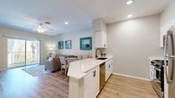 Located in Rancho Cucamonga, CA, this thoughtfully designed single-floor unit maximizes its compact footprint with an open-concept layout that seamlessly connects the kitchen and living areas. Light wood-style flooring runs throughout, lending warmth and visual continuity to the entire space.

The kitchen is a standout feature, equipped with crisp white shaker cabinetry accented by matte black hardware, a quartz peninsula countertop with a built-in undermount sink, and a full suite of stainless steel appliances including a gas range, microwave, and refrigerator. Recessed lighting illuminates the workspace efficiently, while the peninsula provides an ideal spot for casual dining or meal prep.

The living area flows naturally from the kitchen and is brightened by a sliding glass door that opens to a balcony, inviting natural light and outdoor views into the space. A ceiling fan overhead contributes to a comfortable environment year-round. Neutral wall tones serve as a versatile backdrop, complemented by coastal-inspired décor accents in teal and soft blue hues.

A dedicated closet provides practical storage, rounding out the functional layout. Overall, this space offers a clean, modern aesthetic with a welcoming ambiance — ideal for those seeking efficient, stylish living in Southern California.
