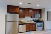 Located at 1249 Griswold Street in the heart of Detroit's downtown, this efficiently designed single-floor unit offers a well-organized layout that maximizes every square foot. The space includes an entrance, a combined dining and kitchen area, a bathroom, a laundry area, a closet, and an additional living area with notable city views.

The kitchen is thoughtfully appointed with rich dark wood cabinetry featuring sleek hardware, gray stone countertops, a stainless steel undermount sink, and a full suite of stainless steel appliances including a refrigerator, electric range, over-the-range microwave, and dishwasher. Recessed lighting illuminates the space efficiently.

The living area is a standout feature, anchored by large black-framed windows that frame striking views of Detroit's surrounding historic architecture, filling the room with natural light and providing a strong urban connection.

The bathroom is finished with consistent dark wood cabinetry, a single vanity with a stone countertop, a frameless glass walk-in shower, and decorative tile flooring that adds texture and character to the space.

A light-toned tile floor runs throughout, contributing to a clean, cohesive aesthetic. The hallway connects each area efficiently, with sliding panel doors and recessed overhead lighting maintaining a modern, streamlined feel throughout the unit.
