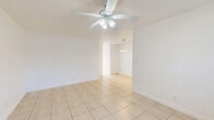 Located at 1860 SW 68th Ave in Miramar, FL, this one-bedroom, one-bathroom unit offers a compact and efficiently designed single-floor layout. Light beige ceramic tile flooring runs consistently throughout every room, lending a clean, cohesive look to the entire space. The living room is a bright, open area featuring a ceiling fan with light fixture, a wall-mounted air conditioning unit, and a window fitted with horizontal blinds that allows natural light to filter in. The space flows openly toward the kitchen, which is a standout feature of the unit, showcasing white cabinetry, granite-look countertops, a decorative mosaic tile backsplash, and stainless steel appliances including a range, microwave, and additional natural light from a window above the counter area. The bedroom is a generously proportioned space that includes a ceiling fan, a sliding double-door closet, a wall AC unit, and a window overlooking the exterior. The bathroom is finished with full white ceramic wall tile surrounding a shower/tub combination, complemented by a window that provides natural ventilation and light. Throughout the unit, crisp white walls and consistent flooring create a bright, neutral palette well-suited for a variety of interior styles.