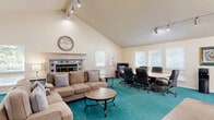 Located at 4121 Dale Rd in Modesto, California, this single-floor space offers a well-appointed and multifunctional layout designed to accommodate both collaborative work and relaxed gatherings. The standout architectural feature is the dramatically vaulted ceiling, which soars overhead and lends a sense of openness and grandeur to the interior. Track lighting runs along the ceiling, providing flexible and ample illumination throughout.

The living area is anchored by bold teal carpeting that extends across most of the floor, creating a vibrant visual focal point. A comfortable lounge zone features a neutral-toned sofa complemented by round wooden side tables, ideal for informal meetings or casual seating. Adjacent to the lounge, a conference area is equipped with a round table and ergonomic office chairs, making it well-suited for professional gatherings.

A decorative fireplace with colorful tile accents adds warmth and character to the space. Multiple windows fitted with white shutters allow generous natural light to filter in, while a sliding glass door provides direct access to the outdoors. A tiled entryway area with built-in cabinetry and a skylight offers a welcoming transition into the main space. Framed artwork displayed on the walls adds a curated, professional aesthetic throughout.