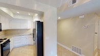 This single-floor residence offers a clean, functional layout designed for comfortable everyday living. The kitchen is a standout feature, outfitted with crisp white cabinetry that provides ample storage, a stainless steel refrigerator, and a sink set beneath recessed lighting that keeps the space well-lit and practical. Light-toned ceramic tile flooring runs throughout, lending a cohesive and easy-to-maintain aesthetic across the home.

An open archway connects the kitchen to the adjacent living area, creating a natural flow between spaces. The neutral, warm beige wall tones throughout the home create a welcoming ambiance that pairs well with the bright, airy feel promoted by the recessed ceiling lights. Wide baseboards add a subtle architectural detail that gives the interiors a polished, finished look.

The ceiling-mounted HVAC vents indicate a central air system, ensuring year-round comfort. The layout makes efficient use of space, with each area transitioning smoothly into the next. Overall, this home presents a tidy and well-maintained interior that balances simplicity with practicality, making it a versatile space suitable for a range of occupants.