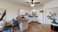 Located at 12025 Paul Eells Dr in North Little Rock, Arkansas, this one-bedroom, one-bathroom residence offers a thoughtfully designed single-floor layout that maximizes every square foot. The open-concept living and kitchen area serves as the heart of the home, where wood-style flooring flows seamlessly underfoot and a ceiling fan with light kit anchors the space above. Large windows invite generous natural light into the living room, offering views of the surrounding exterior. The kitchen is well-equipped with white cabinetry, dark granite-style countertops, a full suite of white appliances including a range, built-in microwave, dishwasher, and refrigerator. A peninsula with bar seating provides a casual dining option and defines the transition between the kitchen and living area. The bedroom offers a comfortable retreat with plush carpeting, a ceiling fan, and a window that continues the theme of natural light throughout the unit. It connects directly to the bathroom and an adjoining closet, creating a practical and private suite. The bathroom features wood-style flooring and clean white cabinetry. Throughout the residence, neutral warm tones and consistent finishes create a cohesive, inviting atmosphere suited for everyday living.