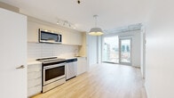 Located in the heart of Montréal, this contemporary one-bedroom, one-bathroom unit at 1020 Rue de Bleury offers a thoughtfully designed open-concept layout with clean, modern finishes throughout. Light hardwood flooring flows seamlessly across the living areas, complemented by striking exposed concrete ceilings that lend an industrial character to the space.

The kitchen is efficiently appointed with sleek cabinetry, white subway tile backsplash, stainless steel appliances including a range, microwave, and dishwasher, and track lighting overhead. It opens directly into the living area, which benefits from floor-to-ceiling windows and a glass door leading to a balcony with panoramic views of the Montréal skyline.

The bedroom is a bright, well-proportioned retreat featuring a tall window with city views, exposed concrete ceiling details, and a generous walk-in closet with built-in hanging storage. The bathroom is finished with large-format tiles, a sleek integrated vanity with a wide mirror, and a glass-enclosed walk-in shower with a rain showerhead. A dedicated in-unit laundry closet with a stacked washer and dryer adds everyday convenience. The hallway entry provides a practical transition into the living space.
