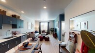 This single-floor residence is designed with a contemporary aesthetic that balances bold color choices with clean, functional design. The open-concept living and dining area serves as the heart of the unit, where light wood-look flooring flows seamlessly throughout. A striking teal accent wall anchors the living space, complementing neutral white walls and providing a vivid backdrop for the entertainment area. Natural light enters through multiple windows dressed with blinds and curtain panels, brightening the space throughout the day.

The kitchen runs along one wall and features dark cabinetry with sleek hardware, stainless steel appliances including a refrigerator, range, microwave, and dishwasher, and light countertops. A compact dining table with bar-style seating sits adjacent, creating an efficient and connected eat-in area.

The bedroom offers plush carpeting, a generously sized window, and access to a walk-in closet. A dedicated built-in workspace with floating shelves and a desk provides a practical nook for productivity. The bathroom includes dark vanity cabinetry, a round mirror, and a combined tub and shower. Recessed lighting and a cohesive color palette tie the entire unit together with a polished, modern feel.