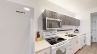 Located at 310 N Jefferson Ave in Springfield, Missouri, this single-floor studio unit offers a clean, modern aesthetic with a highly functional open-concept layout. The space is accessed through a secure entry door and flows seamlessly from the kitchen into the living and sleeping areas.

The galley-style kitchen is a standout feature, equipped with white lower cabinetry, contrasting gray upper cabinets with sleek hardware, white quartz-style countertops, a stainless steel sink, and a full suite of appliances including an electric range, over-the-range microwave, refrigerator, and dishwasher. Light wood-look flooring runs throughout, contributing to a cohesive and bright atmosphere.

The open living and sleeping area is illuminated by natural light from a window fitted with blinds and is topped with a ceiling fan. A freestanding open shelving unit serves as a creative room divider, subtly separating the sleeping area from the living space while maintaining an airy, connected feel.

The bathroom is well-appointed with a gray vanity, white countertop, a large mirror, and a shower-tub combination with a decorative curtain, all finished in a crisp, neutral palette.

Throughout the unit, white walls and light flooring create a bright, welcoming ambiance well-suited for modern urban living in downtown Springfield.