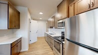 This well-designed 2-bedroom, 1-bathroom unit is laid out on a single floor, making efficient use of its compact footprint. Light wood-tone laminate flooring runs consistently throughout all rooms, creating a cohesive and clean aesthetic that unifies the space.

The kitchen is a functional galley-style space outfitted with warm-toned wood cabinetry, white countertops, and a full suite of stainless steel appliances, including a refrigerator, electric range, and over-the-range microwave. A dedicated area adjacent to the kitchen accommodates a stacked washer and dryer unit, providing convenient in-unit laundry. A hallway with recessed lighting connects the main living areas to the bedrooms.

The primary bedroom is a comfortable, well-proportioned room featuring a window with blinds that allows natural light. The second bedroom is similarly appointed, with windows overlooking surrounding rooftops. Both rooms feature neutral wall tones that complement the light flooring.

The bathroom includes a full soaking tub with shower, a window for natural ventilation, and light wood flooring carried over from the rest of the unit. A dedicated closet provides additional storage. The overall ambiance is clean, modern, and move-in ready.
