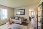 This single-floor residence offers a thoughtfully arranged layout that balances comfort and functionality throughout. The living room serves as the heart of the home, featuring rich hardwood-style flooring, a tiled fireplace with a wall-mounted television above, and large windows fitted with vertical blinds that invite abundant natural light and views of the surrounding greenery. A oversized framed mirror adorns one wall, enhancing the sense of space and brightness in the room. The open flow connects the living area to a dedicated dining space, creating an ideal setting for both relaxing and entertaining. The kitchen is equipped with warm wood cabinetry, granite-style countertops, a full suite of white appliances, and recessed lighting. A notable feature is the in-unit laundry area, conveniently integrated within the kitchen space and accessible via louvered doors. Two well-sized bedrooms offer plush carpeting, large windows with natural light, and tasteful wall art, providing comfortable and tranquil retreats. The bathroom is clean and functional, complete with a combination tub and shower, wood-style flooring, and a vanity with matching wood cabinetry. Throughout the residence, a neutral color palette creates a cohesive and inviting atmosphere.