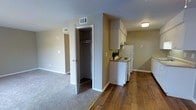 This single-floor residence offers a practical and well-organized layout designed for comfortable everyday living. The open-concept design seamlessly connects the kitchen and living areas, creating a cohesive and functional flow throughout the space.

The kitchen is equipped with white cabinetry, a white electric range, and a full-size refrigerator, all positioned along a dedicated wall. An overhead range hood accompanies the stove, and ample upper cabinet storage ensures plenty of room for kitchen essentials. The kitchen transitions smoothly into the living area, which features rich hardwood-style flooring that adds warmth and character to the space.

A centrally located walk-in closet provides generous storage, making organization straightforward and convenient. The adjacent carpeted area leads to a secondary room, offering versatile use as a bedroom or additional living space. Neutral taupe-toned walls throughout create a calm, neutral backdrop that complements a variety of décor styles.

The space benefits from ceiling-mounted ventilation and recessed HVAC vents for year-round climate control. A textured ceiling and clean white trim add subtle architectural detail. Overall, this residence combines practicality with a straightforward design, making it a functional and move-in ready living space.