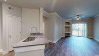 Located at 6141 Avery Dr in Fort Worth, TX, this single-story unit offers a well-designed, open layout with a cohesive blend of modern finishes and functional details throughout. The main living area features rich wood-look flooring, crown molding, and a distinctive teal accent ceiling with a ceiling fan, lending a touch of character to the space. Built-in arched shelving flanks one wall, providing both display and storage opportunities, while a sliding glass door fills the room with natural light and opens to a private patio area.

The kitchen is appointed with white cabinetry, stainless steel appliances including a range, microwave, and refrigerator, along with a peninsula that includes a deep stainless steel sink with an industrial-style faucet. Light wood-look tile flooring and track lighting complete the practical yet stylish kitchen space. A dedicated dining area nearby features warm wood-look flooring and an elegant pendant chandelier.

The bedroom offers plush carpeting, a ceiling fan, and a window overlooking lush greenery, creating a calm and comfortable retreat. The bathroom is finished with large-format textured tile surrounding a soaking tub and shower combination, complemented by wood-look flooring and brushed nickel fixtures. Overall, the space presents a clean, updated aesthetic throughout.