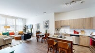 This model unit in Alexandria, Virginia presents a thoughtfully designed two-bedroom, three-bathroom layout that makes efficient use of its single-floor footprint. The open-concept kitchen and living area serves as the heart of the home, featuring warm wood-toned cabinetry extending to the ceiling, granite countertops, stainless steel appliances, and a peninsula with bar seating that flows naturally into the dining and living spaces. Hardwood-style flooring runs throughout the main living areas, complementing the clean, neutral palette and crisp white walls.

The living room benefits from large windows that invite substantial natural light and offer views of the surrounding neighborhood. The primary bedroom is a comfortable retreat with carpeted flooring, notably tall ceilings, and direct access to a dedicated closet with built-in shelving. The secondary bedroom also features generous windows with sheer drapery, enhancing the bright, airy feel. Three well-appointed bathrooms include granite-topped vanities with wood cabinetry and subway-tiled shower surrounds with glass enclosures. A hallway connects the private sleeping quarters to the main living area, and two closets provide practical storage solutions throughout the unit.