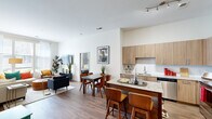 This model unit in Alexandria, Virginia presents a thoughtfully designed two-bedroom, three-bathroom layout that makes efficient use of its single-floor footprint. The open-concept kitchen and living area serves as the heart of the home, featuring warm wood-toned cabinetry extending to the ceiling, granite countertops, stainless steel appliances, and a peninsula with bar seating that flows naturally into the dining and living spaces. Hardwood-style flooring runs throughout the main living areas, complementing the clean, neutral palette and crisp white walls.

The living room benefits from large windows that invite substantial natural light and offer views of the surrounding neighborhood. The primary bedroom is a comfortable retreat with carpeted flooring, notably tall ceilings, and direct access to a dedicated closet with built-in shelving. The secondary bedroom also features generous windows with sheer drapery, enhancing the bright, airy feel. Three well-appointed bathrooms include granite-topped vanities with wood cabinetry and subway-tiled shower surrounds with glass enclosures. A hallway connects the private sleeping quarters to the main living area, and two closets provide practical storage solutions throughout the unit.