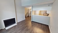 This two-story residence offers a thoughtfully designed layout that balances open living areas with comfortable private spaces. The main level centers around a spacious living room distinguished by dramatically vaulted ceilings, creating an airy and expansive atmosphere. A classic white-surround fireplace serves as a focal point, while rich dark hardwood-style flooring runs throughout the lower level. A sliding glass door floods one area with natural light and provides access to an outdoor space, complemented by a high clerestory window above.

The kitchen is efficiently arranged with crisp white shaker cabinetry, light grey subway tile backsplash, white quartz countertops, and stainless steel appliances including a range with built-in microwave. A pass-through counter connects the kitchen to the living area, enhancing the open-concept feel.

A staircase with white railings leads to the upper level, where plush carpeting runs through the bedrooms. Each bedroom features a ceiling fan with light fixture, soft neutral wall tones, and chair-rail detailing. One bedroom benefits from an interior window overlooking the stairwell, adding architectural interest. The upper level also includes a full bathroom with a soaking tub and shower combo, clean white tile, and a vanity with stone-style countertop.