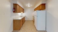 This 1-bedroom, 1-bathroom residence is thoughtfully arranged on a single floor, offering a functional and comfortable layout throughout. The living area is generously sized, featuring wall-to-wall neutral carpeting that adds warmth underfoot. Natural light enters through a multi-pane window, while a wall-mounted air conditioning unit and baseboard heating ensure year-round climate control. An open sightline connects the living space to the kitchen, providing an airy, connected feel. A structural column partially divides the living zone, adding subtle architectural definition to the open plan.

The galley-style kitchen is efficiently designed, featuring warm-toned wood cabinetry that extends to the upper walls for ample storage. A double-basin sink, light countertops, and tile flooring complement the white appliances, including a full-size refrigerator and a range. Recessed overhead lighting keeps the kitchen well-lit throughout the day.

The bedroom is a quiet, carpeted retreat with clean white walls and ample natural light filtering in. The full bathroom is finished with classic white tile surrounding the tub-shower combination, a wood-vanity with an integrated sink, and tile flooring, offering a clean and practical design. Overall, this unit presents a straightforward, well-maintained living space suited for comfortable everyday living.