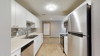 Located at 9825 Centennial Rd in La Vista, Nebraska, this single-floor unit offers two bedrooms and two bathrooms within a well-organized layout. The galley-style kitchen is a functional highlight, featuring white cabinetry, a mosaic tile backsplash, light wood-style flooring, a double-basin sink, and a full suite of stainless steel appliances including a range, over-the-range microwave, dishwasher, and refrigerator. The kitchen opens toward a carpeted hallway that connects the main living areas. The living room is generously sized, bathed in natural light, and features sliding glass doors that lead to a private balcony with pleasant outdoor views of surrounding greenery. Both bedrooms are carpeted and equipped with ceiling fans and textured ceilings; the primary bedroom offers a dedicated window framed in warm wood trim, while the second bedroom also benefits from natural light. The two bathrooms include wood-look flooring and clean, simple fixtures. A stacked washer and dryer unit is conveniently located within the home, adding to everyday functionality. Warm wood trim throughout, neutral wall tones, and consistent finishes give the space a cohesive and practical character throughout.