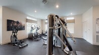 Located at Kerry Park in Delaware, Ohio, this single-floor fitness center offers a comprehensive and well-organized workout facility designed to support a wide range of exercise routines. The space is finished with durable rubber flooring throughout and benefits from abundant natural light streaming in through multiple windows adorned with decorative valances, creating a bright and welcoming environment. Recessed lighting supplements the natural light, ensuring the facility is well-lit at all times of day.

The cardio zone is generously equipped with multiple treadmills, elliptical trainers, and a recumbent bike, several of which feature personal display screens. A wall-mounted television provides additional entertainment for cardio workouts. The strength training area houses a multi-functional cable machine, offering a variety of resistance exercises in one unit. A dedicated free weights section includes a full rack of dumbbells alongside an adjustable weight bench, catering to users of all fitness levels.

A separate functional training area features stability balls, medicine balls, resistance bands, and additional training accessories, with a large wall mirror enhancing the sense of space and allowing for form checks. Interior windows connect this zone to an adjacent lounge or clubhouse area, adding a social and community-oriented feel to the overall facility.