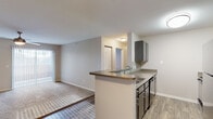 This single-floor residence offers a thoughtfully designed layout that balances functionality and comfort throughout. The open-concept kitchen serves as a central hub, featuring gray cabinetry, a dark countertop peninsula with an integrated sink, black appliances including a full-size refrigerator, and wood-look flooring that extends into the adjacent dining and entry areas. The kitchen flows naturally into the living room, which transitions to plush carpeting and is highlighted by a ceiling fan and a sliding glass door that opens to a private balcony, filling the space with natural light.

The bedrooms are generously sized, each finished with soft carpeting, ceiling fans, and ample closet space. One bedroom features a dedicated window that invites in additional natural light. The layout, as visible in the dollhouse view, provides a practical corridor connecting all private spaces.

Two full bathrooms serve the residence, each equipped with a tub-shower combination, a vanity with storage, and clean, neutral finishes. The hallway connecting the bedrooms is well-lit and lined with additional closet and storage access. Throughout the space, a consistent neutral color palette of warm beiges and soft grays creates a cohesive, move-in-ready aesthetic.