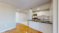 Located at 8200 Wisconsin Avenue in the heart of Bethesda, MD, this two-bedroom, one-bathroom residence offers a well-designed layout with a bright and open feel throughout. Gleaming parquet hardwood floors extend across the living areas and bedrooms, adding warmth and character to the space.

The open-concept kitchen is outfitted with stainless steel appliances — including a gas range, built-in microwave, and full-size refrigerator — complemented by white cabinetry, a white subway tile backsplash, and a dark countertop peninsula that serves as a natural divider between the kitchen and living area. The kitchen floor features elegant marble-look tile.

The living room is generously proportioned, bathed in natural light, and opens to an outdoor balcony through floor-to-ceiling sliding glass doors, offering expansive views of the Bethesda cityscape. The spacious primary bedroom continues the parquet flooring and includes a large window framing scenic elevated views, along with a dedicated walk-in closet featuring built-in shelving and dual hanging rods. The second bedroom also benefits from wide windows and its own closet. The bathroom is finished with white subway tile in the tub/shower surround and marble-look floor tile, maintaining a clean, cohesive aesthetic throughout.