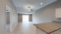 This well-designed single-story home offers a thoughtful open-concept layout that seamlessly connects the main living areas. The living room impresses with vaulted ceilings and a ceiling fan, light wood-look tile flooring, and a sliding glass door fitted with vertical blinds that invites natural light while providing access to the outdoors. The neutral gray walls throughout create a cohesive and modern aesthetic.

The kitchen is a standout feature, equipped with crisp white cabinetry, granite countertops, and a full suite of stainless steel appliances including a refrigerator, range, microwave, and dishwasher. A peninsula counter provides additional workspace and serves as a natural divider between the kitchen and living areas.

The bedrooms offer comfortable, carpeted flooring and ceiling fans. The primary bedroom features a tray ceiling and multiple windows that bring in natural light. Additional bedrooms include ample closet space with double-door closets. The bathroom is well-appointed with white vanity cabinetry, granite countertops, a large mirror, and a walk-in shower with sliding glass doors. Light wood-look tile flooring carries throughout the main living spaces, tying the home together with a clean, contemporary finish.