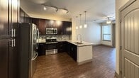 This well-appointed 580-square-foot, one-bedroom, one-bathroom apartment is thoughtfully designed to maximize both style and functionality across a single floor. The open-concept kitchen serves as a centerpiece, showcasing dark espresso cabinetry, granite countertops with a mosaic tile backsplash, and a full suite of stainless steel appliances including a refrigerator, range, and microwave. A peninsula with a built-in sink and pendant lighting above adds both workspace and visual interest, while track lighting and a ceiling fan provide practical illumination. Hardwood-style flooring flows throughout the main living and kitchen areas, adding warmth and continuity. The bedroom spans 160 square feet and features plush carpet, a ceiling fan with light fixture, a window with blinds that allows natural light, and arched panel doors that lend a classic architectural touch. Double doors off the main corridor provide generous closet storage. The bathroom is finished with tile flooring, a granite-topped dark vanity, a framed mirror with vanity lighting, an overhead storage cabinet, and a tiled soaking tub and shower combination. The overall aesthetic is modern yet comfortable, with a cohesive dark-and-light contrast carried throughout the unit.