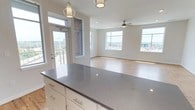 This single-floor residence offers a clean, contemporary design characterized by an open-concept living and kitchen area filled with natural light from large windows framing urban skyline views. The living space features warm hardwood-style flooring, recessed lighting, and a ceiling fan, creating a bright and airy atmosphere. A private entry door leads directly into this open layout, providing a welcoming transition into the home.

The kitchen is well-appointed with white shaker-style cabinetry, open shelving, a white subway tile backsplash, dark granite countertops, and a full suite of stainless steel appliances including a refrigerator, range, microwave, and dishwasher. Decorative pendant lights hang above a central island, adding both style and function.

The bedrooms are carpeted for comfort and each includes a ceiling fan and windows with exterior views. The primary bathroom features a frameless glass walk-in shower and an adjacent built-in closet with wire shelving. A secondary bathroom offers a full tub-shower combination. The unit also includes access to an outdoor balcony, further enhancing the connection to the surrounding cityscape.