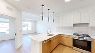 Located at 581 Sayre Ave in Perth Amboy, NJ, this modern two-story home offers 2 bedrooms, 2 bathrooms, a loft, and a balcony, all finished with contemporary design details. The main floor centers on an open-plan kitchen and living area bathed in natural light. The kitchen is a standout, featuring warm wood lower cabinetry paired with crisp white upper cabinets, a textured tile backsplash, stainless steel appliances including a gas range and refrigerator, and a generous island with a white quartz countertop and sleek pendant lighting overhead. Light hardwood flooring flows throughout both levels, contributing to a bright and airy atmosphere. The two bathrooms showcase bold designer tilework — one with vibrant blue subway tiles surrounding a soaking tub and shower, and another with deep green vertical tiles accenting a floating wood vanity with an oval backlit mirror. The bedrooms are spacious and filled with natural light from large windows with neighborhood views, and each benefits from dedicated closet space. A loft area on the upper floor adds flexible living space, while an in-unit laundry room adds everyday convenience. The balcony provides an outdoor retreat, completing this well-appointed, move-in-ready home.