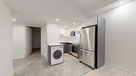 Located at 2121 Rue St-Mathieu in Montréal's vibrant neighbourhood, this two-bedroom, two-bathroom residence offers a thoughtfully designed single-floor layout with modern finishes throughout. The kitchen is outfitted with a full suite of stainless steel appliances — including a French-door refrigerator, built-in microwave, and gas range — complemented by crisp white cabinetry, dark lower cabinets, and light stone-tile flooring. A convenient in-unit washer is integrated directly into the kitchen space. The living and bedroom areas feature light hardwood flooring that lends warmth and continuity throughout the unit. The bedrooms are bright and generously sized, with large windows that frame impressive views of the Montréal city skyline, particularly striking at night. Recessed lighting provides clean, even illumination across all rooms. The two bathrooms offer contrasting aesthetics: one is finished with bold, dark granite-style tiles covering the walls and floor, complete with a soaking tub and shower combination, while the second features elegant white marble-look tile flooring and a sleek floating vanity with a stone countertop and large mirror. Together, these spaces create a functional and stylish urban residence.