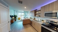 Located at 408 N Terry Ave in the heart of Orlando, FL, this modern single-floor residence blends contemporary urban design with comfortable living. The open-concept layout seamlessly connects the kitchen and living areas, creating a bright, cohesive space bathed in natural light. The well-appointed kitchen is a standout feature, showcasing warm wood-toned cabinetry, granite countertops, a subway tile backsplash, stainless steel appliances, and ambient LED accent lighting that adds a vibrant, modern touch. A peninsula counter extends the workspace and provides a natural transition into the living area. The living space is anchored by large windows that frame city views, allowing generous natural light to fill the room. A glass-panel door opens to a private balcony, further connecting the interior to the outdoors. The bedroom is a serene retreat, highlighted by exposed concrete ceiling and accent wall elements that lend an industrial character, complemented by plush carpeting and a large window with urban views. The bathroom features a wood-grain vanity with granite countertops, a tiled tub-shower combination, and clean, neutral finishes throughout. Light wood-style flooring flows consistently through the main living areas, unifying the space with warmth and continuity.