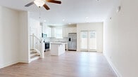 Located at 98 Southport Cir in Brunswick, Georgia, this well-designed two-story home offers three bedrooms and three bathrooms across two thoughtfully laid-out floors. The main level welcomes you through a clean, light-filled entry hallway with light wood-tone flooring that flows throughout the home. The open-concept living area seamlessly connects the living room, dining space, and kitchen, creating an expansive and functional common area. The kitchen is a standout feature, showcasing white shaker-style cabinetry, granite countertops, a central island with bar seating, stainless steel appliances including a gas range, microwave, dishwasher, and French door refrigerator, plus a pantry for added storage. French doors off the living area provide natural light and outdoor access. A staircase with classic balustrades leads to the upper level, where the generously sized primary bedroom features a tray ceiling, ceiling fan, walk-in closet, and a private en-suite bath with a glass-enclosed shower and granite vanity. Two additional bedrooms, a laundry room, and well-appointed bathrooms complete the upper floor. The attached garage offers convenient parking and storage. The exterior presents a charming coastal aesthetic with grey shingle siding and a white garage door.