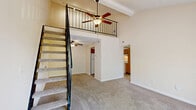 Located at 1509 Moonstone Way in Lyndon, KY, this one-bedroom, two-bathroom apartment spans two floors with a smart, functional layout. The living room immediately impresses with soaring vaulted ceilings, a ceiling fan, and a large sliding glass door that fills the space with natural light and provides views of the surrounding greenery. A striking open-railed staircase leads to a loft above, adding a unique architectural dimension and additional usable space. The main level flows from the carpeted living area into the kitchen, which features warm honey-toned wood cabinetry, ample counter space, a double basin sink, and white appliances including a refrigerator, dishwasher, and electric range. Hardwood-style flooring runs throughout the kitchen and laundry areas. The dedicated laundry room comes equipped with washer and dryer hookups and overhead wire shelving for added storage. The spacious primary bedroom offers plush carpet, a generous closet, and a window overlooking the outdoors. Both bathrooms are clean and functional, with one featuring a full tub-shower combination and tile flooring. A hallway connects the main rooms, completing a well-organized floor plan ideal for comfortable everyday living.