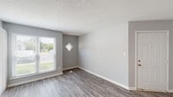 Located at 884 Lakecrest Ave in High Point, NC, this single-floor unit offers a practical and cohesive layout with consistent neutral gray tones and clean white trim throughout. The main living area features wood-style vinyl plank flooring and benefits from natural light provided by a standard window alongside a distinctive diamond-shaped accent window. A dedicated entry door opens directly into this space, lending a sense of arrival and separation from the outside.

The kitchen connects to the living area via a pass-through opening with a breakfast bar-style counter, allowing for an open sightline between the two spaces. It is equipped with white cabinetry, light speckled countertops, a double-basin stainless steel sink, and a full suite of black appliances including a refrigerator, electric range, and over-the-range microwave. A closet and additional storage are accessible just off the kitchen corridor.

The bedroom is finished with plush carpeting, a ceiling fan with light fixture, and a sliding glass door that opens to an outdoor patio, bringing in natural light and exterior views. The bathroom includes a tub and shower combination, a vanity with storage, and wood-style flooring that complements the rest of the unit. Textured ceilings are consistent throughout the space.
