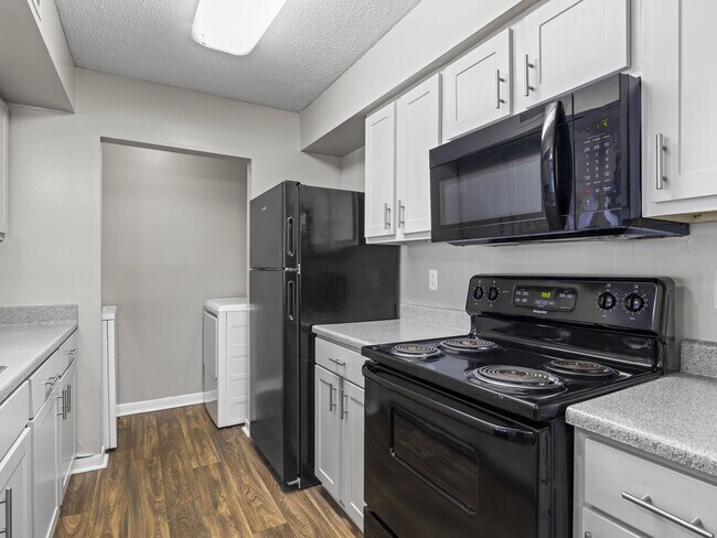 Las cocinas, elegantemente equipadas, cuentan con refrigerador y estufa de color negro, y gabinetes blancos, y son operadas profesionalmente por Highlands Vista Group. - Park at Meadow Ridge