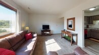 This single-floor residential unit offers a comfortable and practical layout designed for everyday living. The kitchen is a functional highlight, featuring dark taupe cabinetry, light stone-look countertops, and a full suite of stainless steel appliances including an electric range with microwave above, a dishwasher, and a refrigerator. Durable wood-look flooring runs through the kitchen and dining area, where a compact dining set provides a cozy spot for meals.

The living room is generously sized and filled with natural light from a large picture window. Plush carpeting and neutral wall tones create a warm, inviting atmosphere, with ample room for comfortable seating arrangements.

The unit includes multiple bedrooms, each carpeted and finished with clean, neutral walls and sliding or hinged closet storage. Windows in several bedrooms allow for natural light and outdoor views of the surrounding landscape. Each room offers a peaceful, restful environment.

The bathroom features a wide vanity with warm wood cabinetry, a light countertop, a mirrored medicine cabinet with Hollywood-style lighting above, and wood-look flooring that ties cohesively to the rest of the unit.

Throughout the space, textured ceilings, wood trim baseboards, and consistent neutral tones create a unified, understated aesthetic that is both livable and well-maintained.