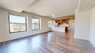 This thoughtfully designed one-bedroom, one-bathroom residence offers a comfortable and functional single-floor layout with an open-concept living and kitchen area. Hardwood-style flooring flows throughout, lending a warm and cohesive aesthetic to the entire space.

The open living room is generously proportioned, bathed in natural light from multiple large windows that frame elevated urban cityscape views. The kitchen is seamlessly integrated into the living area via a peninsula with a light stone countertop, ideal for casual dining or food prep. Rich warm-toned wood cabinetry provides ample storage, complemented by stainless steel appliances including a refrigerator and dishwasher, a single-basin sink, and recessed and pendant lighting overhead.

The bedroom is a comfortable retreat with its own window offering city views, along with access to a dedicated closet featuring built-in shelving for organized storage. The bathroom is clean and functional, appointed with large-format tile surrounding a full tub-shower combination, a wood-toned vanity, and light stone countertop. A hallway and additional closet round out the layout, offering practical storage solutions throughout this well-organized urban residence.