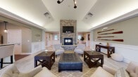 This well-appointed single-story community space offers a thoughtfully designed layout with a variety of functional areas. The centerpiece is a dramatic great room featuring soaring vaulted ceilings, a floor-to-ceiling stacked stone fireplace with a mounted television above, and comfortable seating arranged on a patterned area rug. Wainscoting and sage-green walls lend a refined, cohesive aesthetic throughout, complemented by nautical accents including decorative oars and a compass rose wall piece.

The welcoming entry foyer continues the stone fireplace motif and opens to the main gathering areas via wide, accessible corridors. A dedicated dining area enjoys an abundance of natural light through large windows dressed with patterned draping curtains and tile flooring underfoot. The kitchen is equipped with rich dark cabinetry, granite countertops, stainless steel appliances, and ample storage.

Additional private rooms with carpeted floors and natural window light offer flexible-use spaces. A fully accessible bathroom features grab bars, a roll-in shower, and wood-look tile, prioritizing safety and comfort. The dedicated fitness room is well-equipped with strength training machines, exercise balls, cardio equipment, wall mirrors, and natural light from multiple windows, making it a fully functional wellness space.