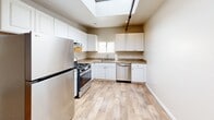 Located in Oakland's Fruitvale neighborhood, this two-floor live/work space blends industrial character with thoughtful residential amenities across a generously sized footprint. The main floor commands immediate attention with its soaring ceilings, dramatic exposed wooden roof trusses, and polished concrete floors that stretch across a wide-open, light-filled interior. Pendant industrial lighting hangs overhead, while a charming sliding barn door adds warmth and rustic character to the otherwise clean, white-walled space. A staircase leads to the upper level, where the residential quarters are tucked away. The bedroom features wall-to-wall carpeting, exposed piping details on the ceiling, a closet with sleek panel doors, and soft sconce lighting that creates a calm, functional retreat. An additional carpeted room with exposed beam accents and track lighting offers flexible use as a studio, office, or lounge. The kitchen is well-appointed with white shaker cabinets, granite countertops, stainless steel appliances including a gas range, dishwasher, and refrigerator, plus a skylight that fills the space with natural light. The bathroom is finished with wood-look tile flooring, a dark wood vanity, and brushed nickel fixtures. Two closets provide ample storage throughout.