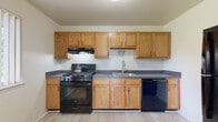 This single-floor unit offers a clean, functional layout with a neutral color palette throughout. The entry opens to a well-lit living area finished with light wood-style flooring that flows seamlessly through the main spaces, creating a bright and cohesive feel. A large window fitted with vertical blinds allows natural light to fill the room, enhancing the open atmosphere.

The kitchen is efficiently designed, featuring warm oak cabinetry extending to the upper walls for generous storage. Dark speckled countertops provide a practical work surface, complemented by a black gas range with hood ventilation, a black dishwasher, and a stainless-steel sink — a complete and functional cooking space.

The bedroom is comfortably sized, carpeted for warmth, and includes a window overlooking greenery outdoors. It connects directly to an en-suite bathroom equipped with oak vanity cabinetry, dark speckled countertops, a wide mirror, and a separate tub area. A second bathroom in the unit mirrors this design with matching vanity finishes and a tub-shower combination, offering added convenience for guests or additional occupants.