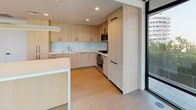 This single-floor residence is designed with a consistent modern aesthetic, characterized by clean lines, neutral tones, and high-quality finishes throughout. Light hardwood flooring flows seamlessly across the living and bedroom areas, contributing to a bright and cohesive interior palette.

The kitchen is a standout feature, outfitted with flat-front light wood cabinetry accented by matte black hardware. Upper and lower cabinets provide generous storage, while a marble-style subway tile backsplash adds texture behind the white quartz countertops. Stainless steel appliances, including a gas range, built-in oven, and microwave, are integrated into the cabinetry. A kitchen island offers additional workspace and casual seating potential. Floor-to-ceiling windows adjacent to the kitchen invite abundant natural light.

The bedrooms are well-proportioned, each featuring large black-framed windows that frame outdoor views of surrounding greenery and urban scenery. One bedroom includes access to an outdoor terrace. Closet space is outfitted with wire shelving and hanging rods for practical storage.

The bathrooms are finished with large-format dark grey floor tiles and marble-style wall tile. One bathroom features a glass-enclosed walk-in shower, while another includes a soaking tub with a glass shower enclosure, a light wood vanity, white quartz countertop, and integrated under-mount sink.