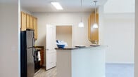 Located in West Columbia, SC, this well-appointed one-bedroom, one-bathroom residence offers a thoughtfully designed single-floor layout with a functional and inviting flow throughout. The kitchen is fully equipped with warm honey-toned cabinetry, granite-style countertops, black appliances including a refrigerator, range, and built-in microwave, and durable wood-look flooring. A curved breakfast bar with elegant pendant lighting opens directly to the living area, creating a natural connection between cooking and entertaining spaces. Crown molding adds a refined touch to the living area, which features plush carpeting and a ceiling fan set beneath a raised tray ceiling. The generously sized bedroom is filled with natural light from a large window overlooking greenery, and includes a ceiling fan and soft carpeting. A dedicated closet provides ample storage. The full bathroom features wood-look flooring, a vanity with granite-style countertops, warm cabinetry, and a tub-shower combination. A dedicated in-unit laundry area with overhead shelving adds everyday convenience. A hallway connects the spaces cohesively, completing this efficiently designed and comfortable home.