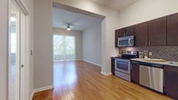 This single-floor residence offers a thoughtfully designed open-concept layout that seamlessly connects the kitchen and living areas. Rich hardwood flooring flows throughout the main living spaces, reflecting natural light and lending warmth to the interior. The kitchen is well-equipped with dark espresso cabinetry, granite-style countertops, a full suite of stainless steel appliances including a French door refrigerator with ice dispenser, electric range, built-in microwave, and dishwasher, all accented by a mosaic tile backsplash. Track lighting overhead enhances functionality and ambiance. The living area opens to a sliding glass door fitted with vertical blinds, providing access to an outdoor view and filling the space with natural light. A ceiling fan adds comfort to this airy room. The bedroom features plush wall-to-wall carpeting, a large window with outdoor views, and generous wall space. The bathroom is finished with large-format tile flooring, a dark vanity with a granite-style countertop, and a well-lit mirror. Throughout, neutral tones and clean architectural lines create a cohesive, modern aesthetic.