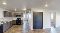 This single-story home in Union, Box Elder, South Dakota, offers a practical and efficiently designed layout accommodating four bedrooms and two full bathrooms within a compact footprint. The interior features a consistent, contemporary aesthetic throughout, with neutral tones, recessed lighting, and a clean, move-in-ready condition.

The kitchen is equipped with dark-stained cabinetry, light granite-style countertops, and black appliances including a refrigerator, range with over-the-range microwave, and dishwasher. Wood-look plank flooring runs through the kitchen and main living areas, lending warmth and durability to the space.

Both bathrooms feature tub/shower combinations with curved curtain rods, tile-style flooring, dark vanity cabinetry, and granite-style countertops, providing a cohesive look. The dedicated laundry room includes shelving and accommodates a full-size washer and dryer.

The bedrooms are carpeted and finished with neutral walls, offering comfortable, functional spaces. Windows in the bedrooms frame views of the surrounding South Dakota landscape. A wood-railed deck extends the living space outdoors, providing expansive, unobstructed views of open fields and distant hills under wide-open skies.