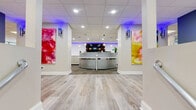 Located at 110 North 17th Street in St. Louis, MO, this single-floor leasing office is a thoughtfully designed, open-concept space that blends professional functionality with vibrant creative energy. The interior features light wood-look flooring throughout, a suspended tile ceiling with recessed and panel lighting, and crisp white walls that serve as a bright, clean backdrop for the space's bold artistic accents.

Upon entry, guests are greeted by a welcoming reception area with a sleek white desk, display signage, and easy access to the main floor. The open layout flows seamlessly into a comfortable lounge zone, anchored by a large sectional sofa, colorful abstract area rug, and a dramatic full-wall mural in vivid swirls of orange, pink, and gold — an immediate visual centerpiece. Adjacent to the lounge is a dining-style meeting area with a round table and upholstered chairs, ideal for client consultations.

A glass-walled private meeting room offers a semi-enclosed workspace with seating and a round accent rug, providing both transparency and privacy. A dedicated workstation area with a desk, monitor, and ergonomic seating supports day-to-day office operations. Ambient blue accent lighting near a display niche adds a modern, polished touch. Natural light filters in through vertical-blind windows, further enhancing the bright, energetic atmosphere throughout.