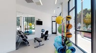 Located at 2202 S Kinnickinnic, this modern fitness facility is designed with a clean, minimalist aesthetic that creates an open and energizing environment for exercise. The single-floor layout is defined by crisp white walls, speckled rubber flooring, and large floor-to-ceiling windows framed in bold black trim, flooding the interior with abundant natural light and offering clear views of the surrounding streetscape.

The facility is divided into well-appointed workout zones. A dedicated cardio area houses multiple Spirit treadmills and an elliptical trainer, accompanied by a wall-mounted flat-screen television. The strength and functional training area features a dumbbell rack, weight benches, a recumbent exercise bike, and an extensive collection of medicine balls, stability balls, resistance bands, and yoga mats neatly organized on freestanding racks. A large wall mirror in this zone enhances the sense of space and supports proper form during workouts.

The entry area includes a minimalist seating nook with a modern white chair alongside expansive windows, creating a welcoming transition into the facility. A restroom is conveniently accessible from the main workout floor. Linear LED lighting throughout complements the natural light, ensuring the space remains bright and inviting at all hours. The overall design balances functionality and contemporary style, making this an efficient and well-equipped fitness destination.
